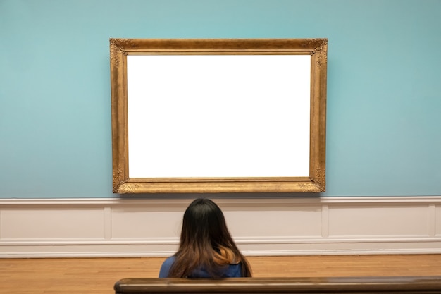 Photo spectateur à la recherche d'un grand cadre doré vierge sur un mur bleu dans une galerie d'art