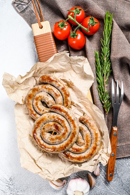 Spirale de saucisses grillées servie sur une planche à découper. Fond gris.