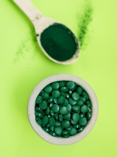 Spiruline hawaïenne verte dans des cuillères à soupe de pilules et de poudre sur fond vert clair