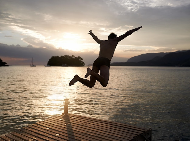 Spontanéité au coucher du soleil Vue arrière d'un jeune homme plongeant de la jetée dans un lac au coucher du soleil