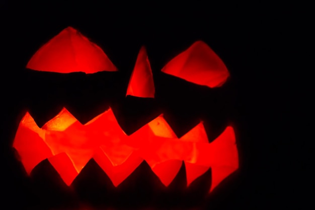 Spooky Jackolantern de citrouille d'Halloween avec des bougies allumées sur fond sombre