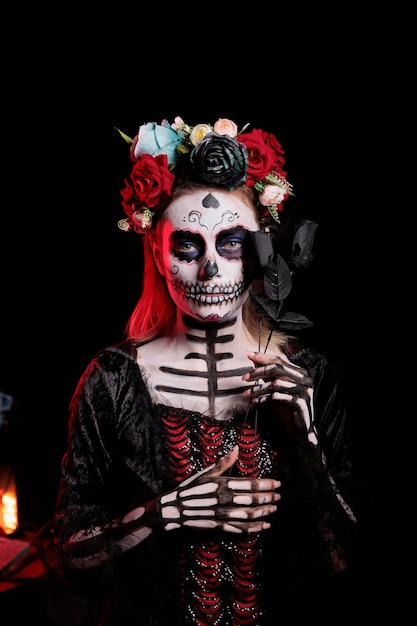 Spooky Lady Of Dead Avec Crâne Et Couronne De Fleurs Colorées Posant En Studio, Utilisant La Rose Noire Pour être Glamour Et Effrayante. Femme Avec Maquillage De Festival Et Costume D'halloween Mexicain.