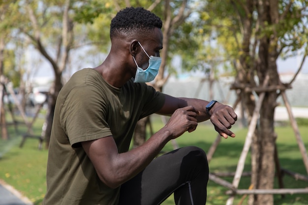 Sport afro-américain vérifiant les performances ou la trace du pouls de la fréquence cardiaque. Sport et fitness en plein air. Les peuples portent un masque chirurgical facial pendant l'épidémie de coronavirus et de grippe