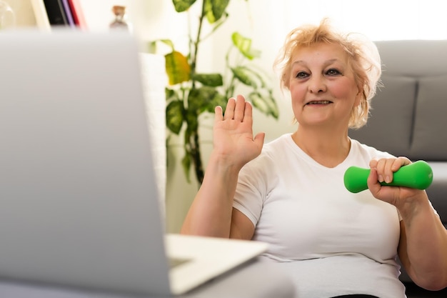 Sport à domicile. Femme âgée active faisant des exercices d'étirement de réchauffement devant un ordinateur portable, s'entraînant avec des didacticiels en ligne.