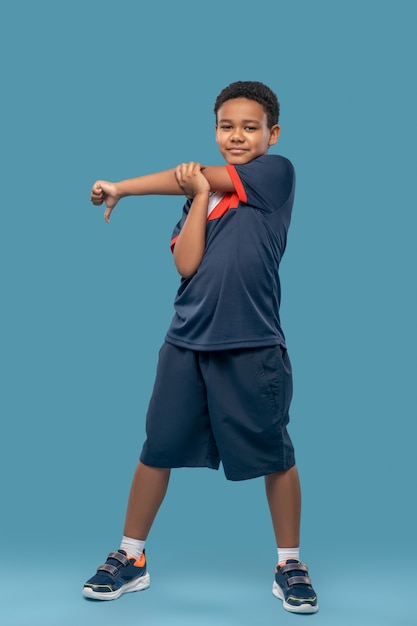 Sport, échauffement. Garçon afro-américain souriant en t-shirt et short de sport debout faisant l'échauffement pour les mains