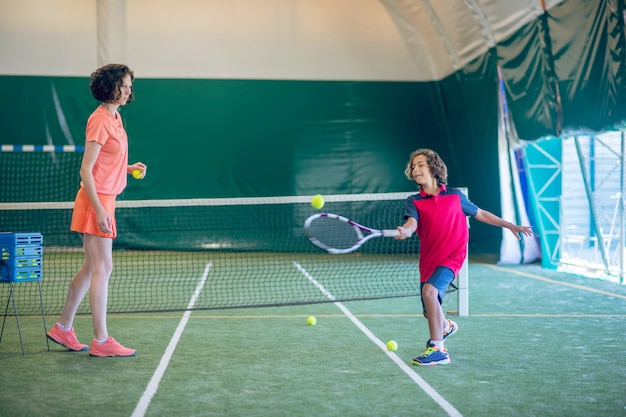 En sport. Entraîneur féminin en vêtements lumineux jouant au tennis avec un garçon