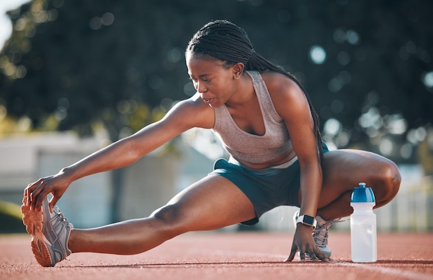 Sport d'exercice et une femme s'étirant à l'extérieur sur une piste pour courir, s'entraîner ou faire de l'exercice. Athlète africain, personne au stade pour étirer les jambes, la forme physique et les muscles, s'échauffer ou faire du bien-être au sol.
