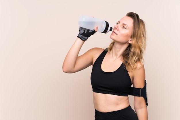 Sport femme blonde sur mur isolé avec bouteille d'eau de sport