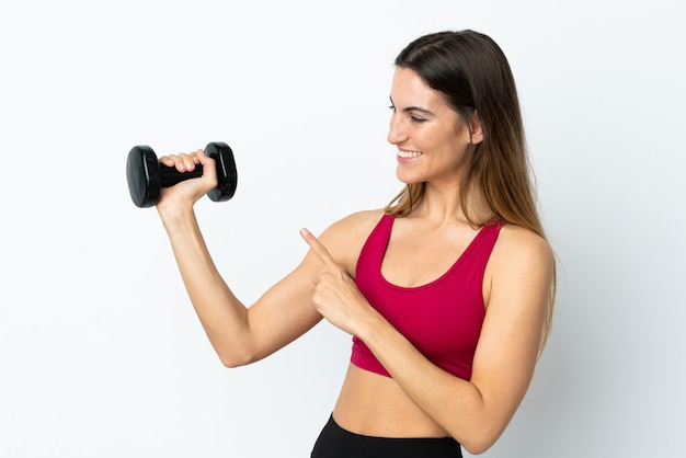 Sport femme faisant de l'haltérophilie sur mur blanc et en le pointant