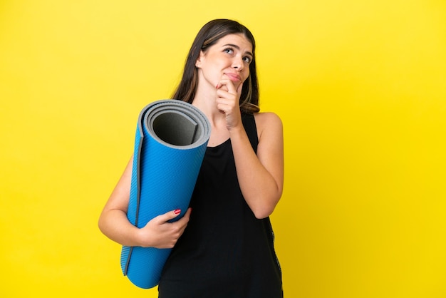 Sport femme italienne allant à des cours de yoga isolé sur fond jaune ayant des doutes