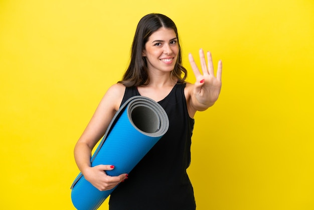 Sport femme italienne allant à des cours de yoga isolé sur fond jaune heureux et comptant quatre avec les doigts