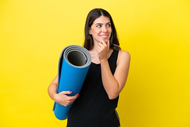 Sport femme italienne allant à des cours de yoga isolé sur fond jaune regardant sur le côté et souriant