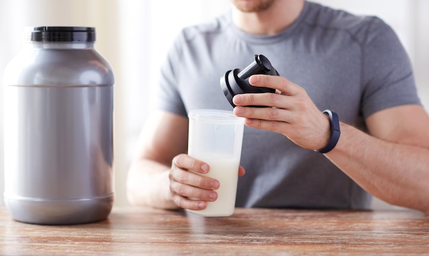 sport, fitness, mode de vie sain et concept de personnes - gros plan sur un homme en bracelet de fitness avec bocal et bouteille préparant un shake protéiné