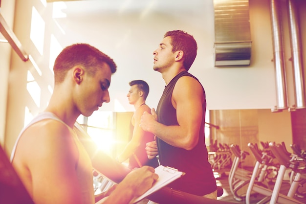 sport, forme physique, mode de vie, technologie et concept humain - hommes avec entraîneur personnel exerçant sur tapis roulant en salle de sport