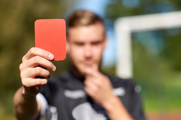 sport, prudence, jeu et personnes - gros plan des mains de l'arbitre avec sifflet montrant un carton rouge sur le terrain de football