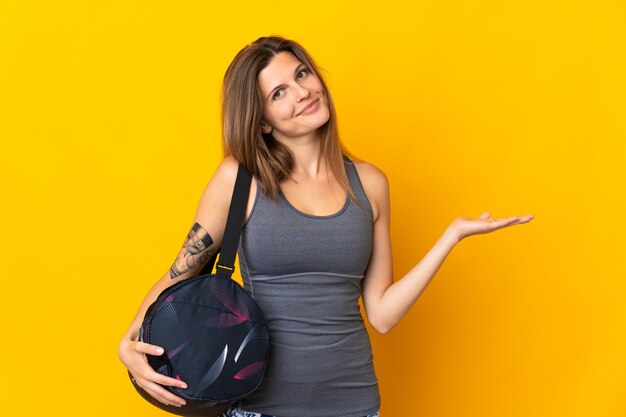 Sport slovaque femme avec sac de sport isolé sur fond jaune étendant les mains sur le côté pour inviter à venir