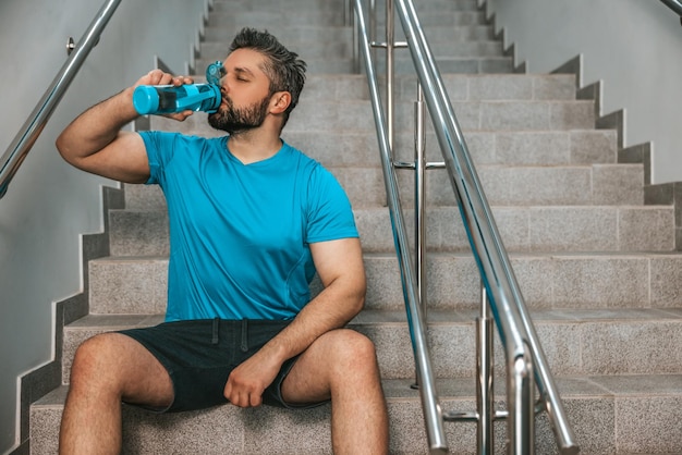 Sportif assis sur les escaliers et boire de l'eau