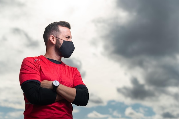 Sportif aux bras croisés portant un masque facial regardant sur le côté.