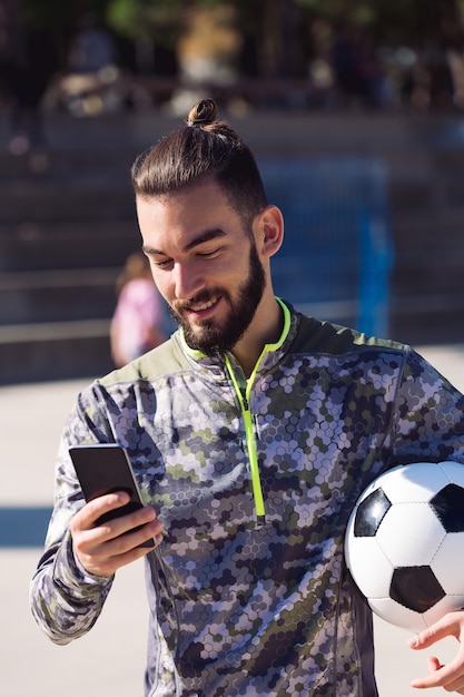 Sportif avec un ballon de football en consultant son téléphone