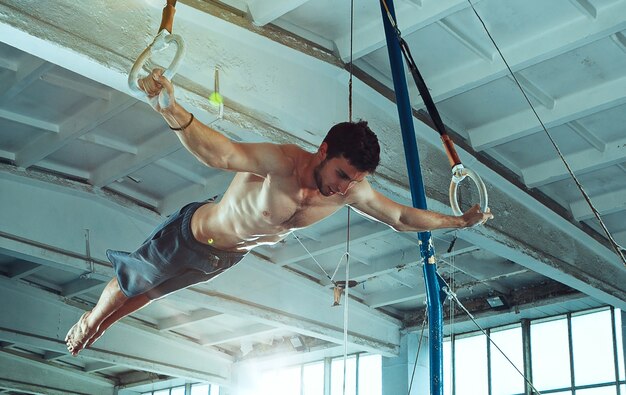 Le sportif effectuant des exercices de gymnastique difficiles au gymnase. Le sport, l'exercice, le gymnaste, la santé, l'entraînement, le concept d'athlète. Modèle de forme caucasienne