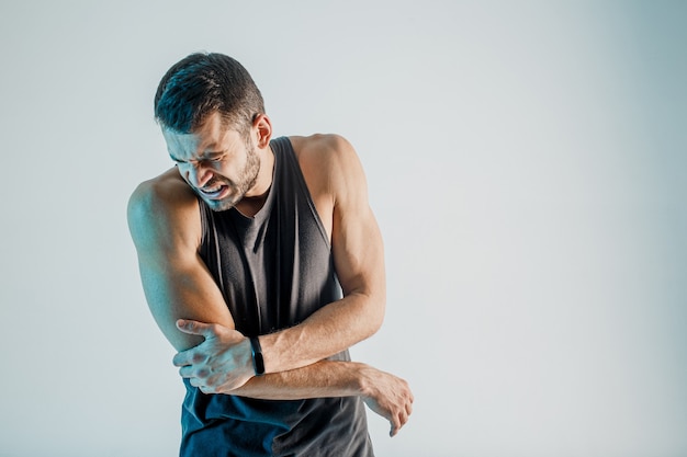 Sportif épuisé ressentant une douleur au coude. Un jeune homme européen barbu porte un uniforme de sport. Concept de blessure sportive. Isolé sur fond turquoise. Tournage en studio. Espace de copie