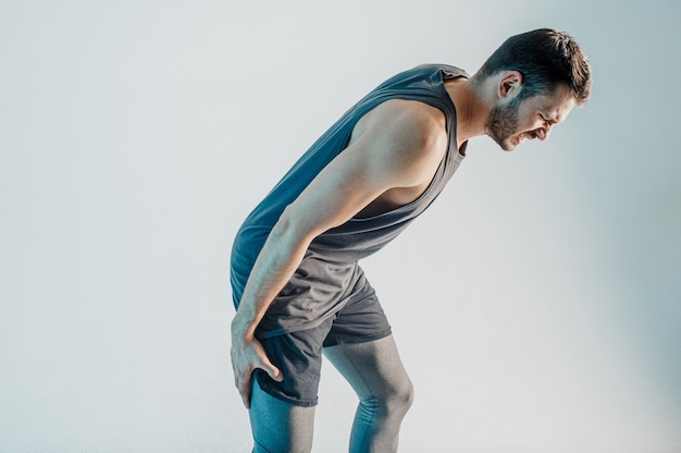 Sportif épuisé ressentant une douleur à la jambe. Un jeune homme européen barbu porte un uniforme de sport. Concept de blessure sportive. Isolé sur fond turquoise. Tournage en studio. Espace de copie