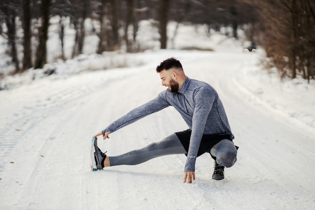 Sportif faisant des exercices d'étirement et se préparant à courir dans la nature lors d'une journée d'hiver enneigée. Vie saine, forme d'hiver