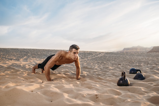Sportif faisant des exercices de push-up dans le désert à la journée ensoleillée. Forte motivation sportive, musculation en extérieur