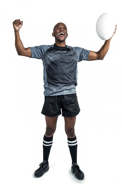 Sportif gai avec poing fermé tenant le ballon de rugby après la victoire debout sur backgroun blanc