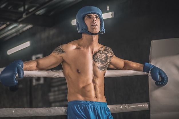 Sportif. Kickboxer avec un tatouage sur la poitrine dans un hemlet bleu