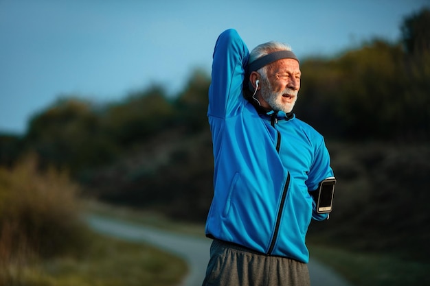 Sportif mature dédié étirant ses bras tout en s'échauffant et en faisant de l'exercice dans la nature Espace de copie