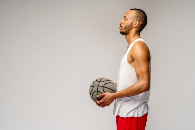 Sportif musclé jouant au basket-ball sur un mur gris clair