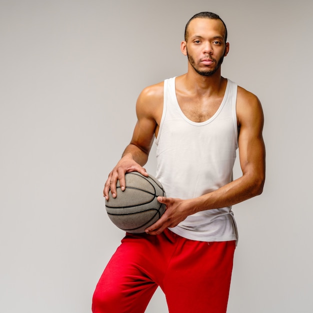 Sportif musclé jouant au basket-ball sur un mur gris clair