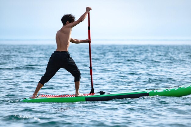 Un sportif nage sur une planche sup avec une pagaie sur la mer pendant la journée contre un beau ciel