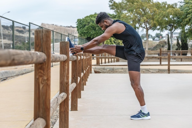 Un sportif noir fait un exercice de toucher les orteils dans le parc.