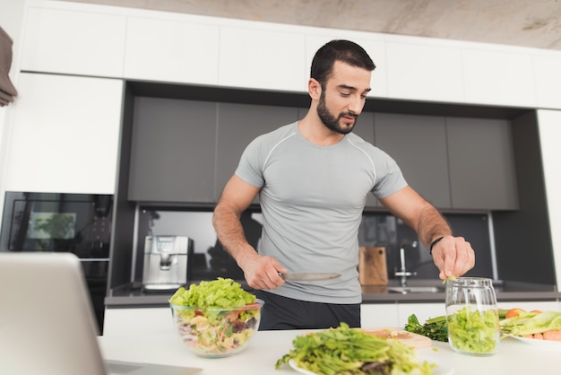 Un sportif prépare une salade dans la cuisine.