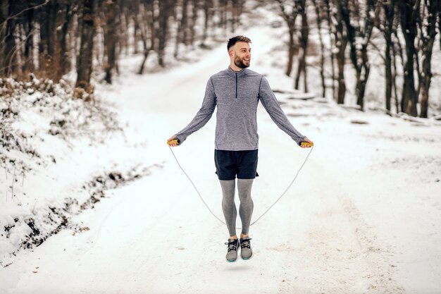 Sportif sautant la corde dans la nature au jour d'hiver enneigé. Fitness d'hiver, vie saine, exercices cardio