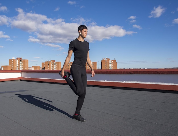 Sportif sportif fort dans les vêtements de sport entraînement d'échauffement faire des exercices d'étirement sur un toit en écoutant