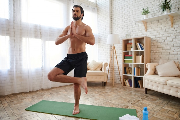 Sportif torse nu pratiquant le yoga avancé à la maison.