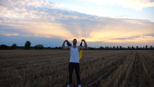 Un sportif ukrainien se tient sur une prairie d'orge montrant des biceps avec une bannière bleu-jaune dans les mains