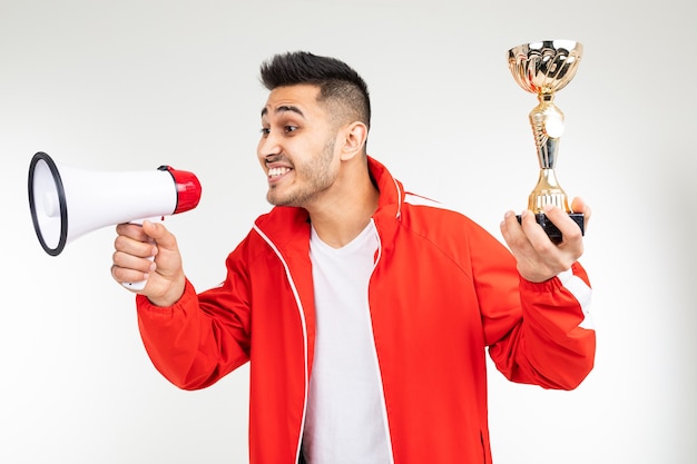 Un sportif en uniforme de sport rouge annonce le vainqueur et tient une coupe d'or sur fond blanc.