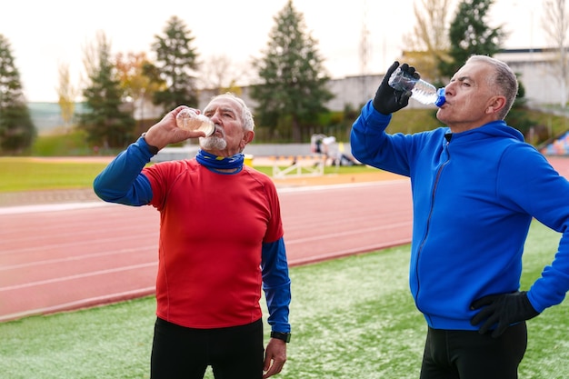 Les sportifs âgés boivent de l'eau tout en faisant une pause après avoir couru sur une piste d'athlétisme