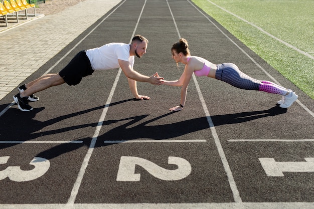 Sportifs, un homme et une femme actifs s'entraînent en été en plein air dans un stade public, ils se tiennent dans la planche et se giflent les mains.