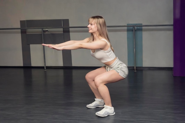 Sportive accroupie Belle fille blonde souriante s'entraîne dans le cul d'entraînement de gym ou les fesses cul élastique fille en short et un t-shirt blanc pour l'entraînement pétrit les muscles des jambes