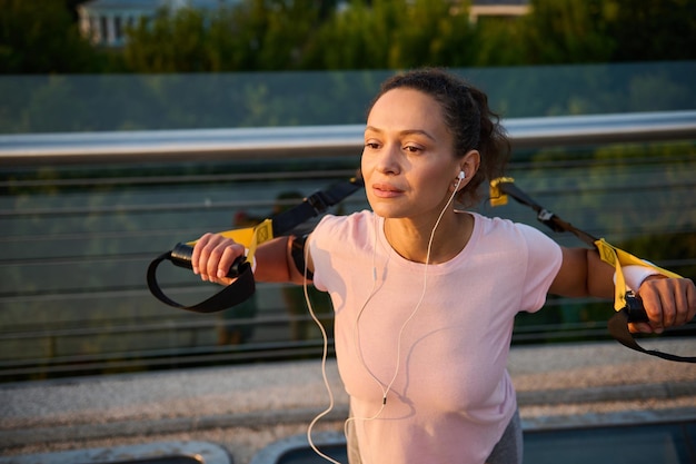 Sportive, athlète féminine déterminée faisant de l'exercice avec des sangles de suspension lors d'un entraînement de poids corporel en plein air au lever du soleil. Femme africaine d'âge moyen sportive travaillant dans une belle journée d'été