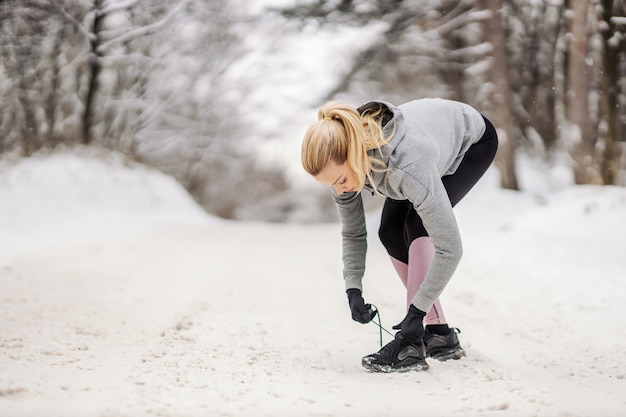 Sportive attachant les lacets en se tenant debout sur le chemin enneigé au jour d'hiver.
