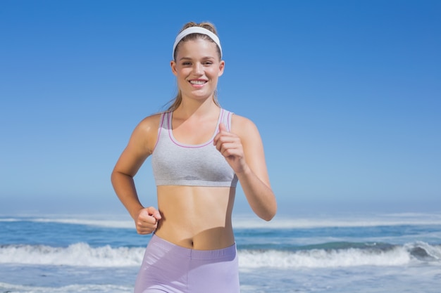 Sportive blonde heureuse jogging sur la plage