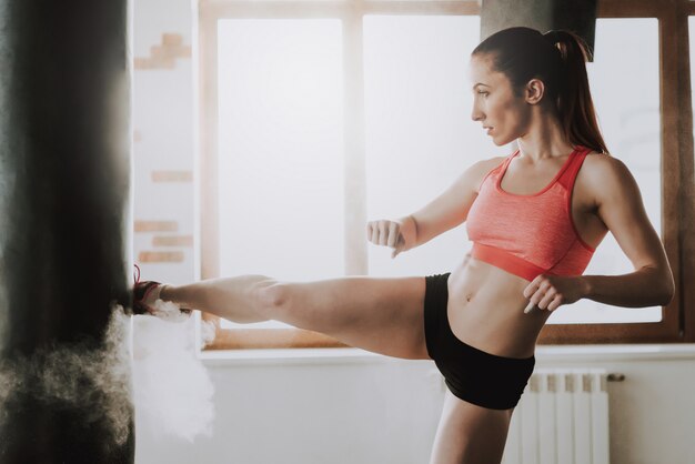 La sportive donne un coup de pied au sac de boxe dans le gymnase