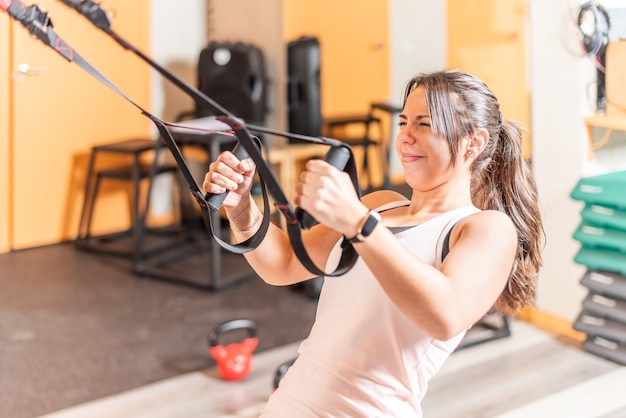 Sportive faisant de l'exercice avec l'expression de la souffrance avec des sangles de fitness trx au gymnase. Concept de formation trx.