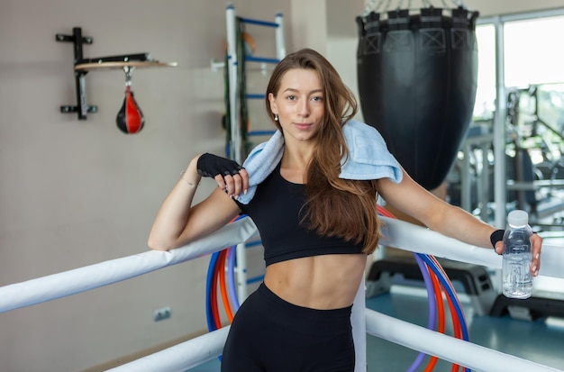 Sportive fatiguée avec une serviette sur ses épaules se reposant dans un ring de boxe